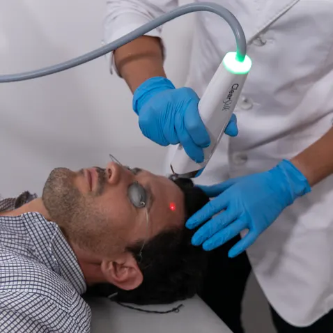 Man receiving ClearSilk™ laser treatment on forehead at Axis Clinic clinic, performed by a professional wearing gloves.