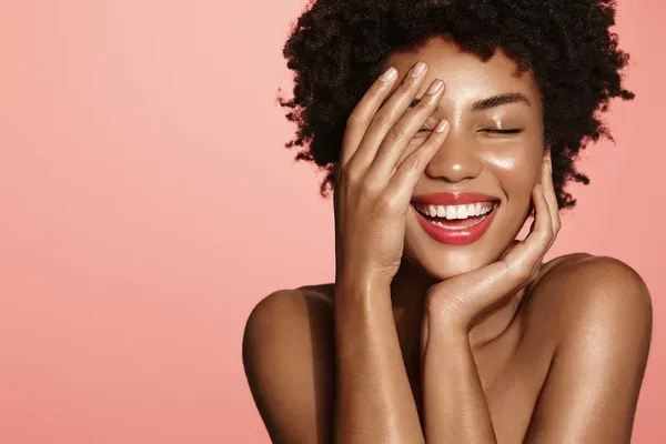 Skin care. Woman with beauty face touching healthy facial skin portrait. Beautiful African girl model with natural makeup touching glowing hydrated skin on pink background closeup